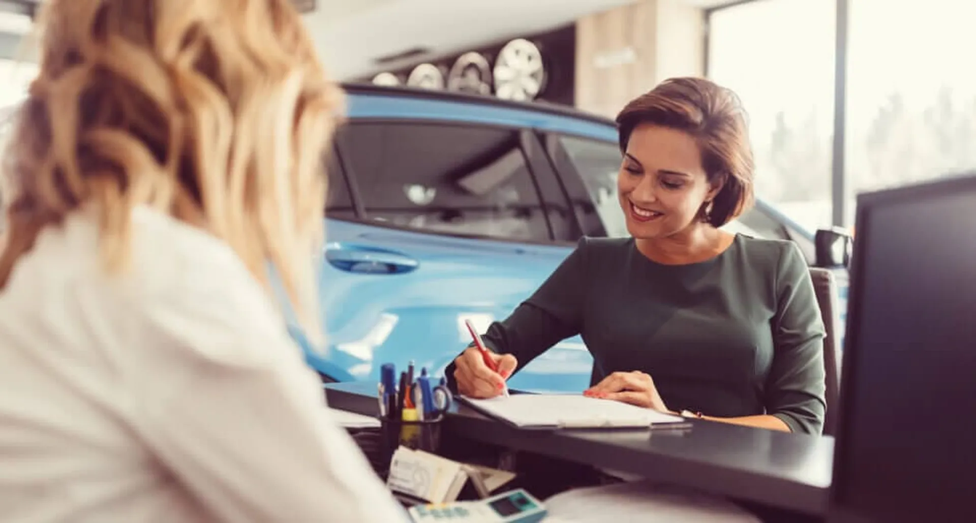 Uśmiechnięta kobieta podpisująca dokumenty na leasing samochodowy dla obcokrajowca.