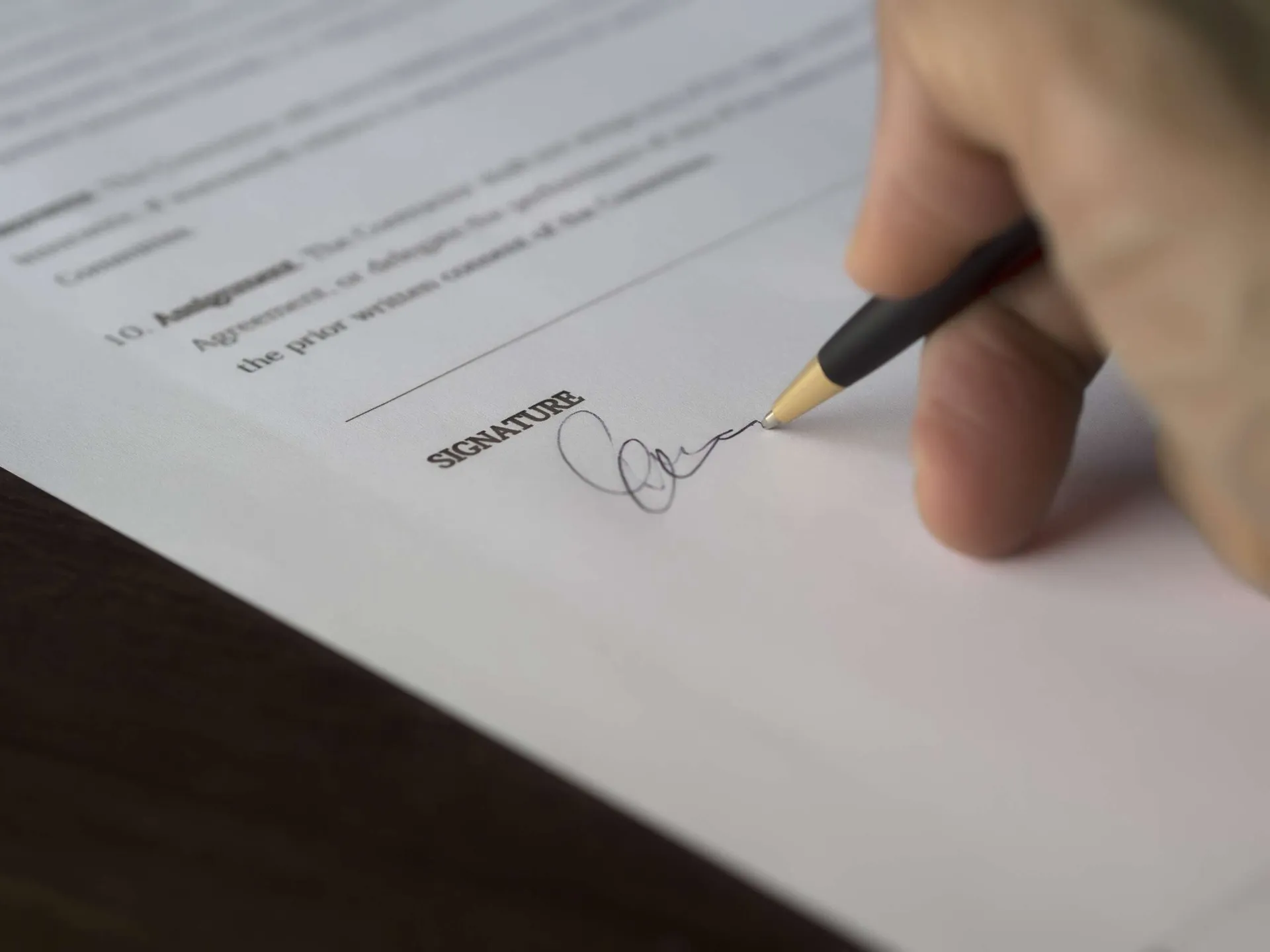 Podpisywanie dokumentu umowy – zbliżenie na dłoń składającą podpis na kartce papieru
